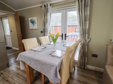 A dining area with a table covered by a patterned cloth and four chairs next to glass doors at Lakeland View Lodge Beckside 2 Limefitt Park near Windermere