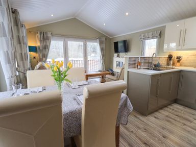 A dining area with a table set with glasses and yellow flowers next to a kitchen with cabinets and a sink at Lakeland View Lodge Beckside 2 Limefitt Park near Windermere