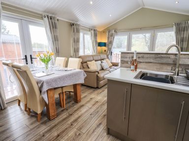 A dining area with a table and chairs next to a living room with a sofa and kitchen sink at Lakeland View Lodge in Beckside 2 Limefitt Park near Windermere