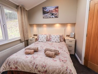 A bedroom with a double bed with butterfly and rabbit patterned bedding two bedside tables with drawers and a window at Lakeland View Lodge in Beckside 2 Limefitt Park near Windermere