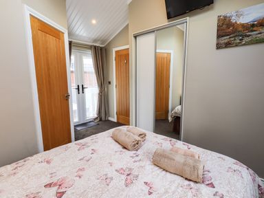 A bedroom with a bed with butterfly patterned bedding two rolled towels on the bed wooden doors glass doors with curtains and a mirrored wardrobe at Lakeland View Lodge in Beckside 2 Limefitt Park near Windermere