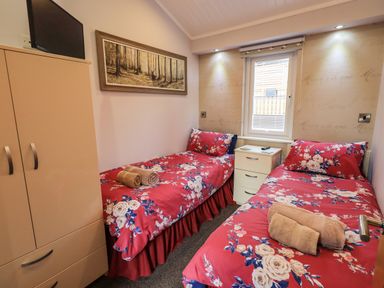 A bedroom with two single beds with red floral bedding a wardrobe and a window at Lakeland View Lodge Beckside 2 Limefitt Park near Windermere