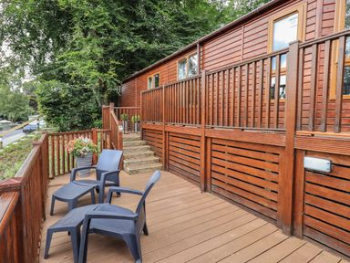 A wooden deck with steps and two black chairs and footrests outside a cabin at Acorn Bank Lodge L 55 Fallbarrow Park near Bowness-On-Windermere