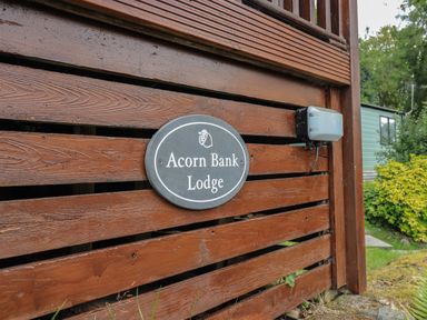 A wooden fence with a sign reading Acorn Bank Lodge near greenery and a building at Acorn Bank Lodge L 55 Fallbarrow Park near Bowness-On-Windermere