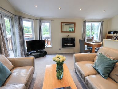 A living room with two sofas a wooden coffee table with flowers a television and dining table at Acorn Bank Lodge L 55 Fallbarrow Park near Bowness-On-Windermere