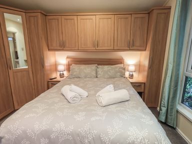 A bedroom with a double bed and wooden cabinets around the bed at Acorn Bank Lodge L 55 Fallbarrow Park near Bowness-On-Windermere