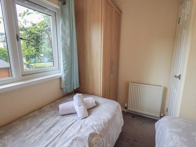A bedroom with two single beds a wooden wardrobe a radiator and a window with curtains at Acorn Bank Lodge L 55 Fallbarrow Park near Bowness-On-Windermere