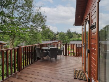 An outdoor wooden deck with a table and chairs surrounded by trees at Acorn Bank Lodge in L 55 Fallbarrow Park near Bowness-On-Windermere