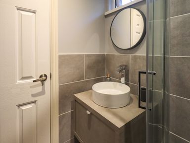 A bathroom with a round mirror round sink faucet and a glass shower door at Acorn Bank Lodge L 55 Fallbarrow Park near Bowness-On-Windermere