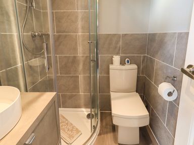 A bathroom with a toilet, a glass shower enclosure, a sink with a cabinet, and tiled walls at Acorn Bank Lodge L 55 Fallbarrow Park near Bowness-On-Windermere
