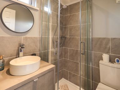 A bathroom with a round mirror above a sink a glass shower enclosure and a toilet at Acorn Bank Lodge L 55 Fallbarrow Park near Bowness-On-Windermere
