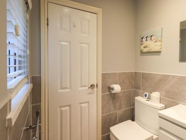 A bathroom with a white door a toilet with toilet paper a wall-mounted toilet paper holder and a small painting at Acorn Bank Lodge L 55 Fallbarrow Park near Bowness-On-Windermere