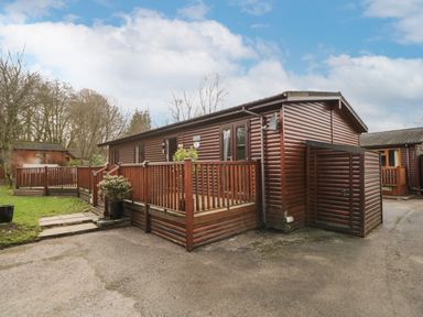 A wooden cabin with a porch and railing next to a driveway and garden at Damson Lodge Thirlmere 8 White Cross Bay Windermere