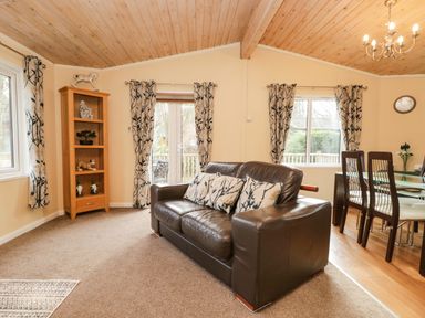A living room with a brown leather sofa and patterned curtains next to a dining table with chairs at Damson Lodge Thirlmere 8 White Cross Bay Windermere