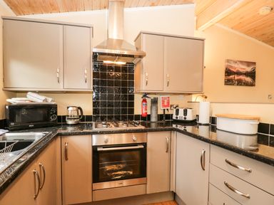 A kitchen with grey cabinets black countertop a microwave kettle gas stove oven and toaster at Damson Lodge Thirlmere 8 White Cross Bay Windermere