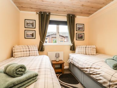 A bedroom with two single beds with plaid bedding and green towels by the window at Damson Lodge Thirlmere 8 White Cross Bay Windermere