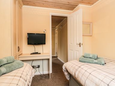 A bedroom with two single beds a TV mounted on the wall and a door open to a hallway at Damson Lodge in Thirlmere 8 White Cross Bay Windermere