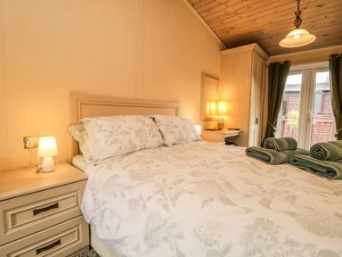 A bedroom with a bed with floral bedding bedside tables lamps a wardrobe and folded towels at Damson Lodge Thirlmere 8 White Cross Bay Windermere