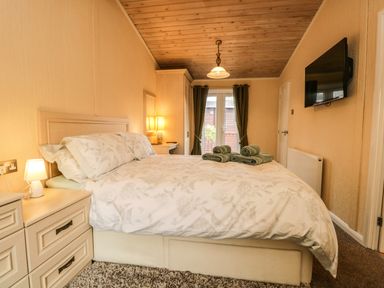 A bedroom with a bed with floral bedding and folded towels on top at Damson Lodge Thirlmere 8 White Cross Bay Windermere