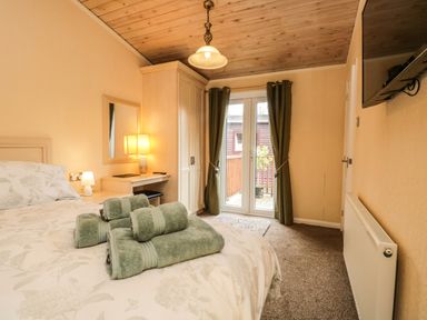 A bedroom with a bed and towels on it a wardrobe a desk with a lamp and mirror green curtains and a wall mounted television at Damson Lodge Thirlmere 8 White Cross Bay Windermere