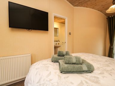 A bedroom with a wall-mounted television folded green towels on a bed and a glimpse of a bathroom at Damson Lodge Thirlmere 8 White Cross Bay Windermere