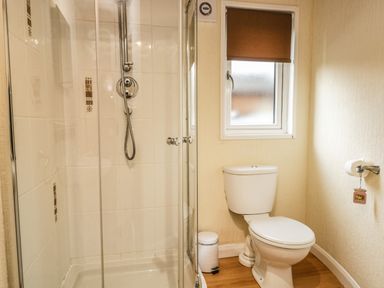 A bathroom with a glass shower enclosure a toilet a small window and a wall-mounted toilet paper holder at Damson Lodge Thirlmere 8 White Cross Bay Windermere