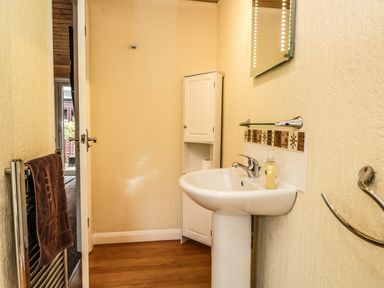 A small bathroom with a pedestal sink a wall cabinet a towel rack with a brown towel and a door leading to another room at Damson Lodge Thirlmere 8 White Cross Bay Windermere