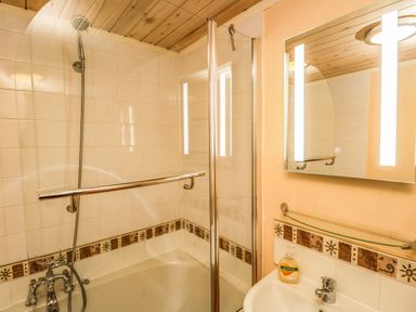 A bathroom with a bathtub shower combination a glass shower screen a mirror above a sink and patterned tiles at Damson Lodge Thirlmere 8 White Cross Bay Windermere