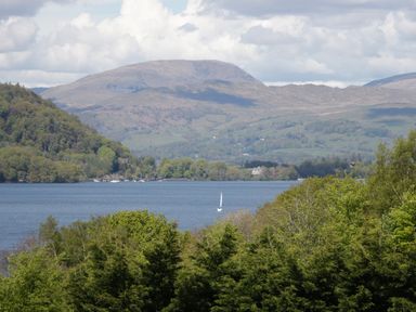 A lake surrounded by green trees with a sailboat on the water and hills in the background at Damson Lodge Thirlmere 8 White Cross Bay Windermere