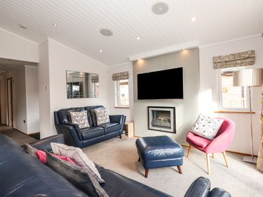 A living room with blue leather sofas a pink chair a wall-mounted tv and a fireplace at Ridgway Lodge Calgarth 40 White Cross Bay near Windermere