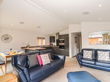 A living room with blue leather sofas and a kitchen with gray cabinets at Ridgway Lodge in Calgarth 40 White Cross Bay near Windermere