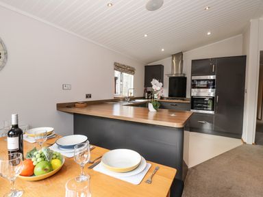 A kitchen with dark cabinets and wooden countertop and a dining table set with plates glasses and fruit bowl at Ridgway Lodge Calgarth 40 White Cross Bay near Windermere