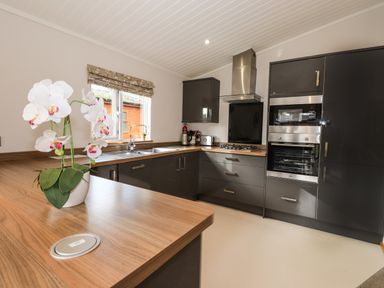 A kitchen with gray cabinets wooden countertops a gas stove an oven a microwave a window and a white orchid on the counter at Ridgway Lodge Calgarth 40 White Cross Bay near Windermere