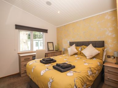 A bedroom with a bed with yellow deer patterned bedding and two folded towels on it a desk under a window and wooden furniture at Ridgway Lodge in Calgarth 40 White Cross Bay near Windermere