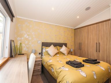 A bedroom with a bed with animal print bedding a desk with green vases and a chair and wooden wardrobes at Ridgway Lodge Calgarth 40 White Cross Bay near Windermere