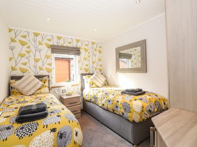 A bedroom with two single beds with yellow sheep patterned bedding a nightstand and a mirror at Ridgway Lodge Calgarth 40 White Cross Bay near Windermere