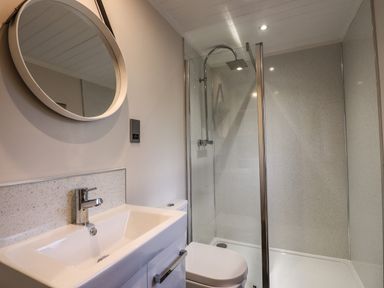 A bathroom with a sink a round mirror a toilet and a glass-enclosed shower at Ridgway Lodge Calgarth 40 White Cross Bay near Windermere