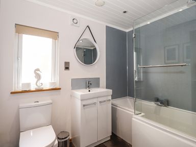 A bathroom with a toilet sink with cabinet bathtub with glass screen and a round mirror at Ridgway Lodge Calgarth 40 White Cross Bay near Windermere