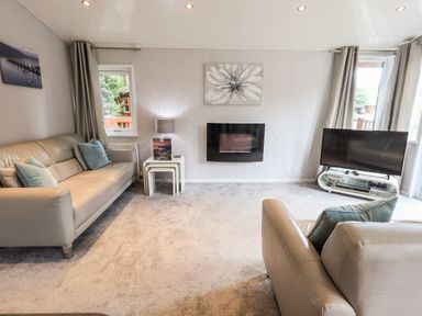 A living room with two sofas a wall-mounted fireplace a television on a stand and grey curtains at Buttermere Lodge Glade 5 Fallbarrow Park near Bowness on Windermere