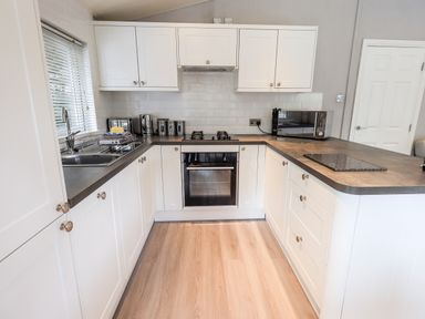 A kitchen with white cabinets black countertop a gas stove oven microwave and sink at Buttermere Lodge Glade 5 Fallbarrow Park near Bowness on Windermere