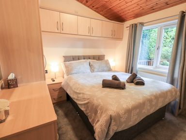 A bedroom with a double bed bedside tables built in cupboards and a window with curtains at Buttermere Lodge in Glade 5 Fallbarrow Park near Bowness on Windermere