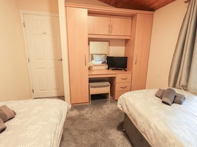 A bedroom with two single beds a wooden wardrobe with a mirror and desk with a small TV at Buttermere Lodge in Glade 5 Fallbarrow Park near Bowness on Windermere