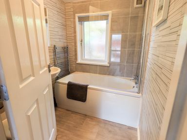 A bathroom with a bathtub a towel rail a window and a small sink at Buttermere Lodge Glade 5 Fallbarrow Park near Bowness on Windermere