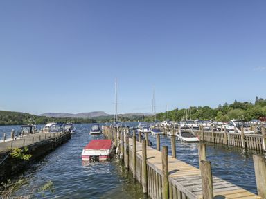 A dock with several boats on a lake surrounded by trees and hills at Rydal Lodge Grasmere 24 White Cross Bay near Windermere