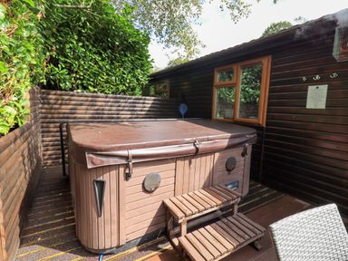 An outdoor hot tub with a brown cover next to a wooden wall and a set of wooden steps at Rydal Lodge Grasmere 24 White Cross Bay near Windermere