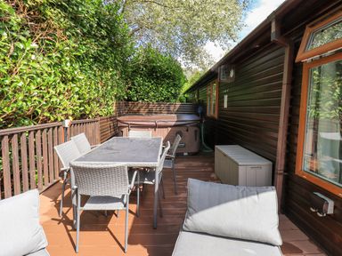 An outdoor patio with a dining table and chairs a hot tub and a storage box at Rydal Lodge Grasmere 24 White Cross Bay near Windermere