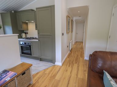 A kitchen with green cabinets and a hallway with wooden floor and brown leather sofa at Wansfell Retreat Lodge Wansfell 4 Limefitt Park near Windermere