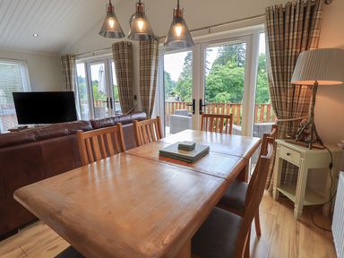 A dining area with a wooden table and chairs beside a balcony door and a living room with a TV and brown sofa at Wansfell Retreat Lodge Wansfell 4 Limefitt Park near Windermere