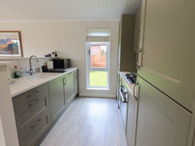 A galley kitchen with green cabinets, a sink with faucet, microwave, and stovetop next to a window at Wansfell Retreat Lodge in Wansfell 4 Limefitt Park near Windermere