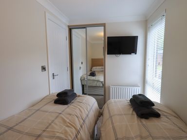 A bedroom with two twin beds towels on the beds a wall mounted TV and a mirrored wardrobe at Wansfell Retreat Lodge Wansfell 4 Limefitt Park near Windermere